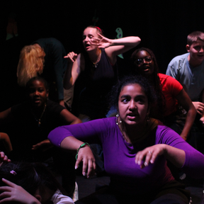 Young people are on a dark stage looking in different directions.