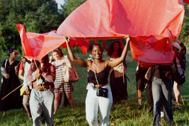 Image of young people under a red scarf in a field